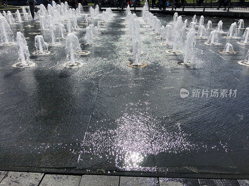 公园花园铺路板上的路面喷水池/湿砖铺路水景，喷水池的水溅在铺路石上，让孩子们在夏天玩耍和淋湿，多个喷水池和水滴倾泻而下